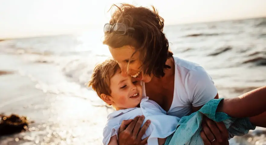 Mama tuli synka na ręce na plaży. To piękny dzień, idealny, by zaplanować wspólne chwile.