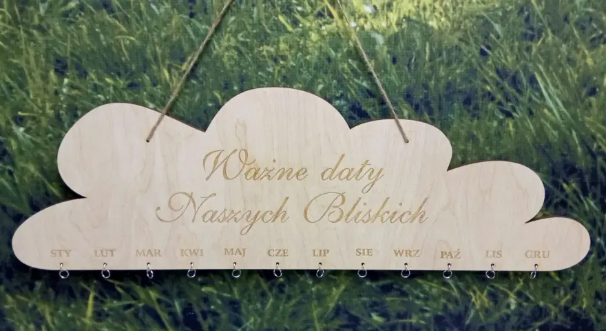 Drewniany kalendarz w kształcie chmurki z napisem "Ważne daty Naszych Bliskich". Poniżej miesiące od STY do GRU, z kółeczkami do zawieszania pamiątek. Idealny do zaznaczania każdego dnia urodzenia.