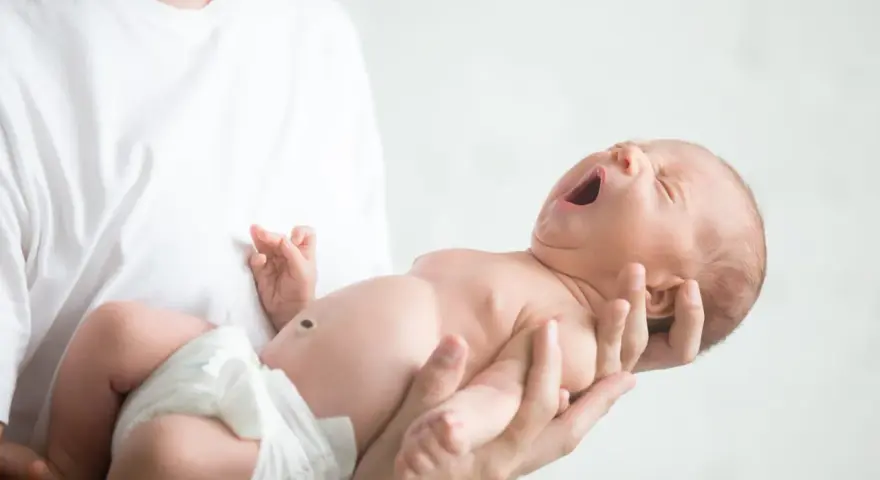 Niemowlę ziewające w ramionach taty. Jedno oko jest lekko przymknięte, drugie otwarte, jakby chciało zobaczyć świat.