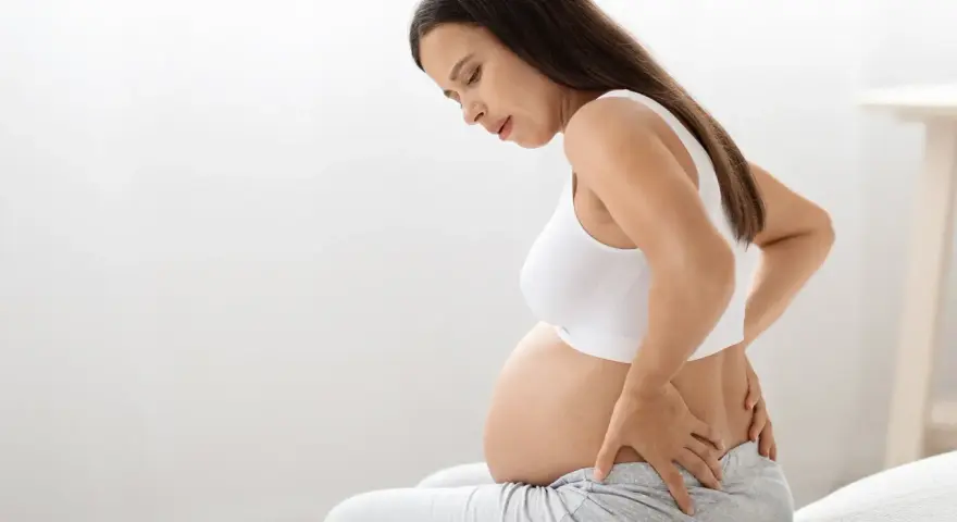 Kobieta w 38 tygodniu ciąży z bólem pleców, trzymająca się za lędźwie.