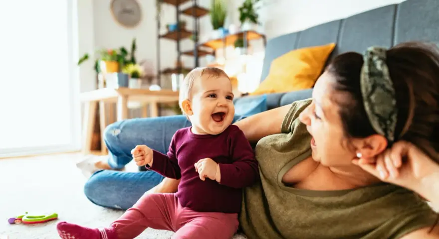 Radosne dziecko 7 miesięcy śmieje się do mamy, leżąc na dywanie.