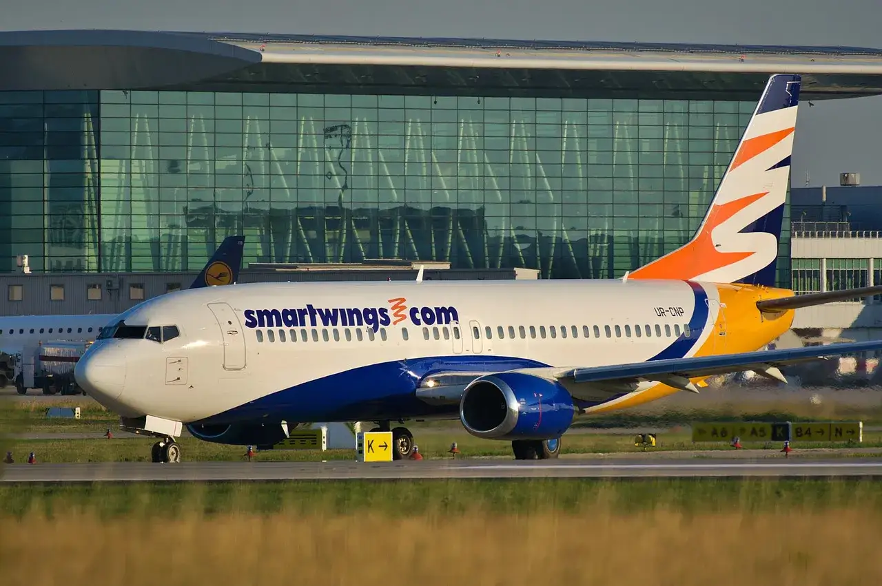 Samolot Smartwings z bagażem rejestrowanym na płycie lotniska przed nowoczesnym terminalem.