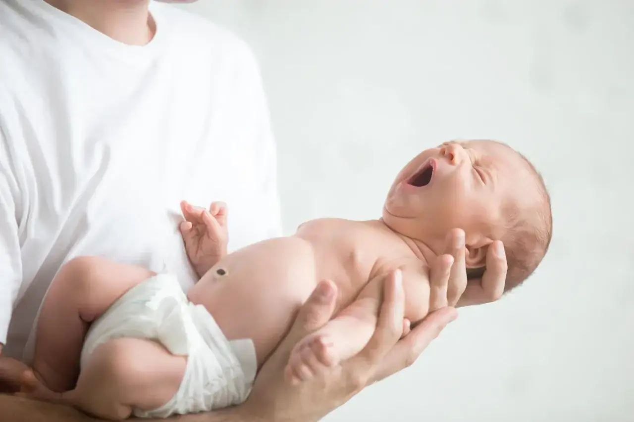 Niemowlę ziewające w ramionach taty. Jedno oko jest lekko przymknięte, drugie otwarte, jakby chciało zobaczyć świat.