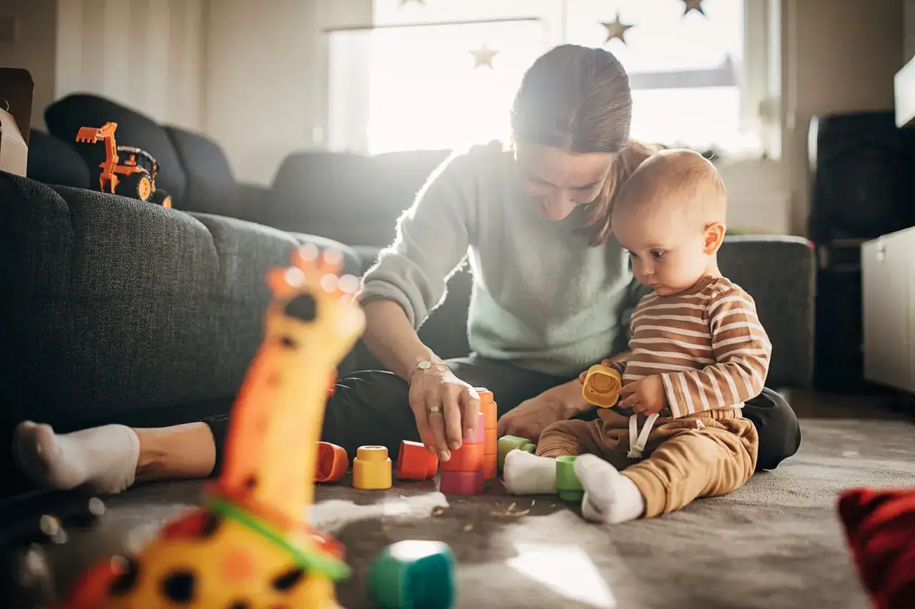 Mama buduje wieżę z klock&oacute;w z dzieckiem 7 miesięcy. Maluch z zaciekawieniem obserwuje zabawę.