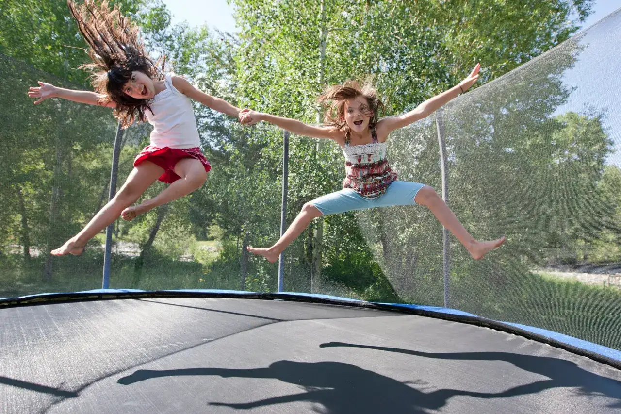 Dwie dziewczynki skaczą na trampolinie, śmiejąc się radośnie. Czy trampolina jest zdrowa dla dzieci? Tak, to świetna zabawa i aktywność fizyczna!